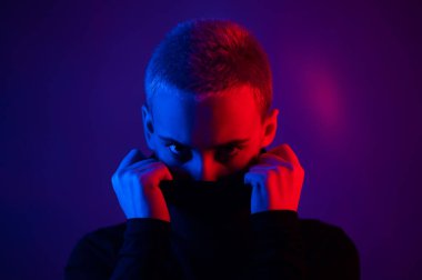 Neon ışıklı kısa saçlı güzel bir genç kadının portresi. Balıkçı yaka giyen bir kız poz veriyor.