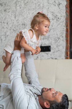 Beyaz bir adam kanepede uzanıyor ve küçük bir kızı üzerinde tutuyor. Şefkatli bir baba çocuğu büyüttü. Mutlu babalar.