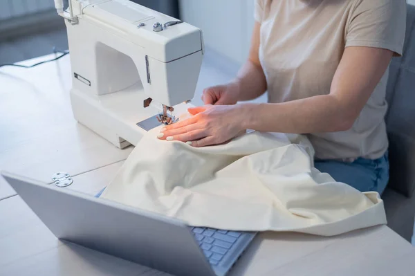Caucasian woman teaches how to sew on a sewing machine from video. Distance education