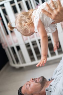 Kafkasyalı adam sırt üstü uzanıyor ve kızını çocuk odasında onun üstünde tutuyor.