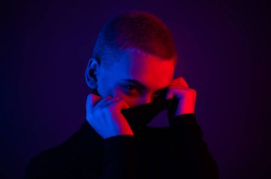 Neon ışıklı kısa saçlı güzel bir genç kadının portresi. Balıkçı yaka giyen bir kız poz veriyor.