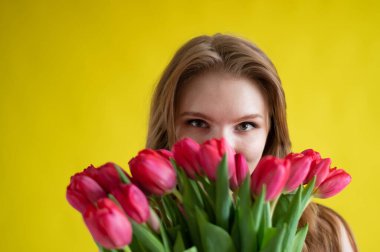 Sarı arka planda kırmızı laleli bir kadın. Siyah elbiseli mutlu kız bir kucak dolusu çiçek tutuyor. Sevgililer Günü için hediye. Yılın en romantik günü..