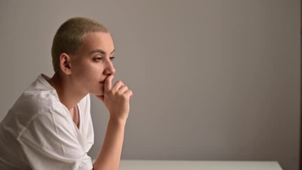 Portret van een trieste jonge vrouw zittend aan een tafel op een witte achtergrond. Kopieerruimte — Stockvideo