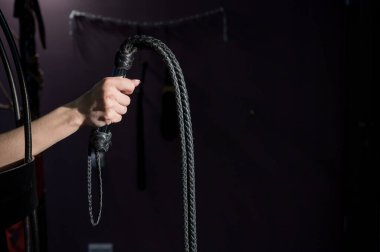 Kafeste uzun, dokunmuş deri kamçılı bir kadın eli. BDSM Ceza ve Zevk. Kırpılmış.