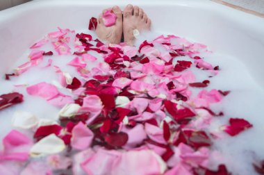 Rahatlatıcı bir banyo yapan bir adamın komik bir fotoğrafı. Erkek ayağının köpüklü ve gül yapraklı bir küvette yakın çekimi.