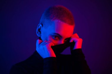 Neon ışıklı kısa saçlı güzel bir genç kadının portresi. Balıkçı yaka giyen bir kız poz veriyor.