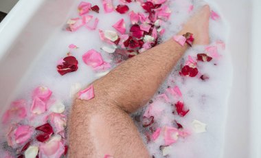 Rahatlatıcı bir banyo yapan bir adamın komik bir fotoğrafı. Erkek ayağının köpüklü ve gül yapraklı bir küvette yakın çekimi.