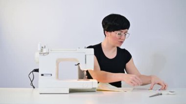 Orta yaşlı bir kadın beyaz arka planda elektrikli dikiş makinesi dikmeyi uzaktan öğretiyor..