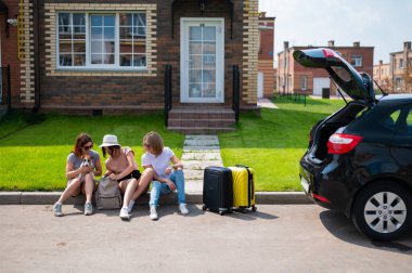 Üç beyaz kadın ve bir köpek bir yolculuğa çıkıyorlar. Kızlar valizlerini arabanın bagajına yüklüyorlar. Kız arkadaşlarla birlikte yaz tatili konsepti.