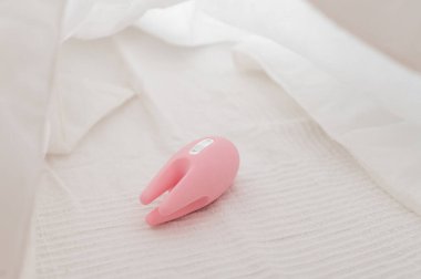 Yatağın üzerinde beyaz bir çarşaf üzerinde klitoral vibratörün yakın çekimi.