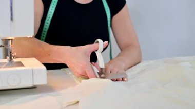 Profesyonel terzi beyaz arka planda makasla malzeme kesiyor. Kimliği belirsiz bir kadın elbise fabrikasında çalışıyor.