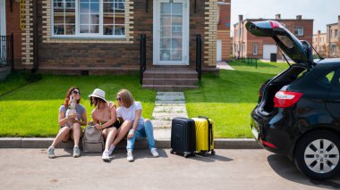 Üç beyaz kadın ve bir köpek bir yolculuğa çıkıyorlar. Kızlar valizlerini arabanın bagajına yüklüyorlar. Kız arkadaşlarla birlikte yaz tatili konsepti.