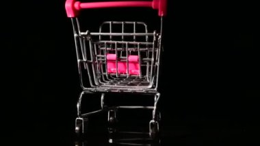 Siyah arka planda dönen pembe saplı boş bir alışveriş arabası..