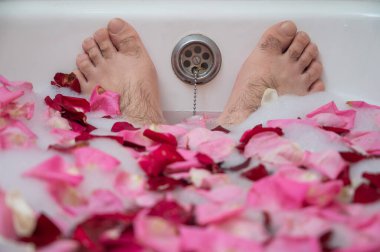 Rahatlatıcı bir banyo yapan bir adamın komik bir fotoğrafı. Erkek ayağının köpüklü ve gül yapraklı bir küvette yakın çekimi.