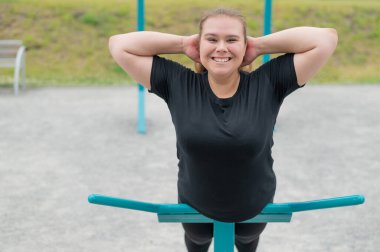 Spor sahasında egzersiz makineleri üzerinde egzersiz yapan şişman genç bir kadın..