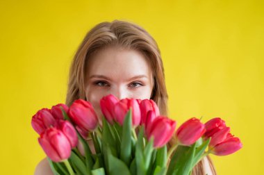 Sarı arka planda kırmızı laleli bir kadın. Siyah elbiseli mutlu kız bir kucak dolusu çiçek tutuyor. Sevgililer Günü için hediye. Yılın en romantik günü..