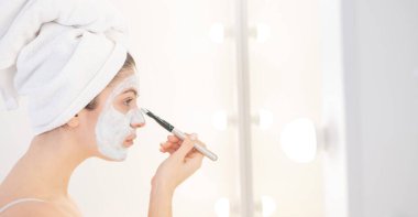 Saçında havlu olan güzel beyaz kadın kilden bir maske takıyor. Evdeki güzellikle ilgilenmek.