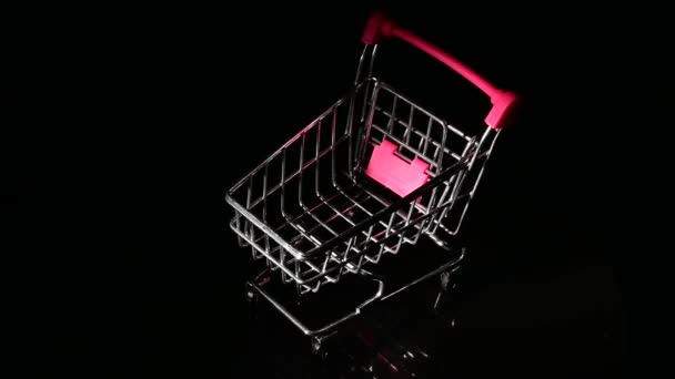 Carro de compras vacío con asa rosa girando sobre fondo negro. — Vídeo de stock