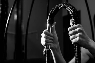 Kafeste uzun, dokunmuş deri kamçılı bir kadın eli. BDSM Ceza ve Zevk. Kırpılmış.