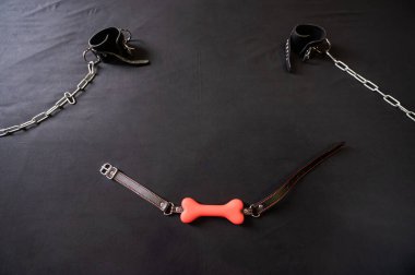 Kemik şeklinde bir şaka ve gri bir çarşafta zincirli deri kelepçeler. BDSM konsepti. Yetişkinler için rol yapma oyunları. Egemenlik ve itaat.