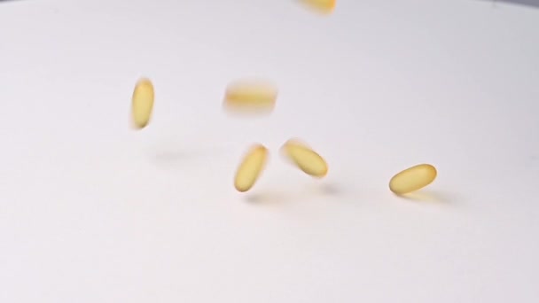 Close-up van vallende transparante gele capsules over een witte achtergrond. Voedingssupplementen met omega 3 en visolie — Stockvideo