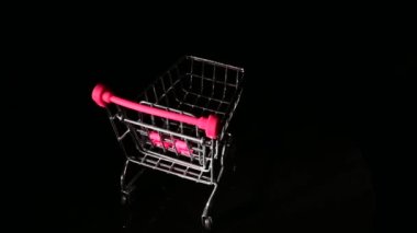 Siyah arka planda dönen pembe saplı boş bir alışveriş arabası..