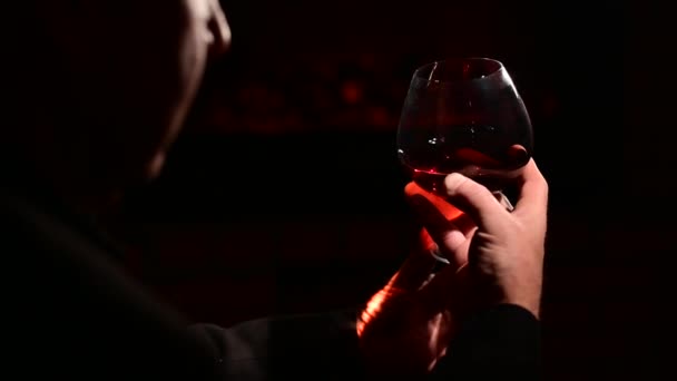 Közelkép egy férfi kezéről egy pohár whiskyvel a kandalló mellett a sötétben. Az elit úriemberek klubjának koncepciója