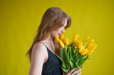 Sarı arka planda sarı lalelerle dolu kolları olan beyaz bir kadın. Uluslararası Kadınlar Günü. Bahar çiçekleri.