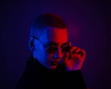 Güneş gözlüklü, kısa saçlı, neon ışıklı güzel bir kadının portresi.