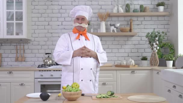 Portret van een oudere mannelijke chef met een dikke grijze snor die zijn handen op zijn buik houdt terwijl hij in de keuken staat — Stockvideo