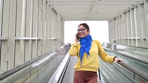 Happy woman stands on a travelator and talks on a cell phone — Stock Video