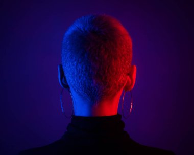 Kısa sarı saçlı, neon ışıklı güzel bir kadın arkasında duruyor..