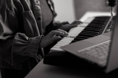 Elektrikli piyanonun kadın ellerine yakın çekim. Bir kadın dizüstü bilgisayarda sentezleyici çalmayı öğreniyor.