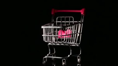 Siyah arka planda dönen pembe saplı boş bir alışveriş arabası..