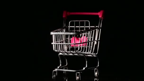 Carro de compras vacío con asa rosa girando sobre fondo negro. — Vídeo de stock