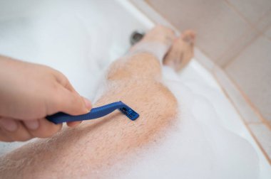 Rahatlatıcı bir banyo yapan ve bacaklarını tıraş eden bir adamın komik bir fotoğrafı. Köpük banyosunda erkek ayağının yakın çekimi. Üst görünüm.