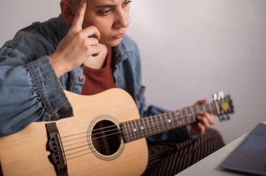 Genç kadın internette gitar çalmayı öğreniyor. Dizüstü bilgisayarda uzak müzik dersleri