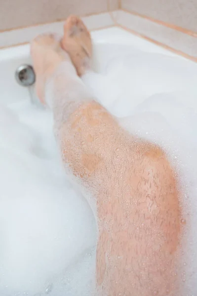 Funny picture of a man taking a relaxing bath. Close-up of male feet in a bubble bath