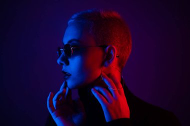 Güneş gözlüklü, kısa saçlı, neon ışıklı güzel bir kadının portresi.