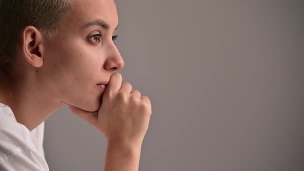 Portret van een trieste jonge vrouw zittend aan een tafel op een witte achtergrond. Kopieerruimte — Stockvideo