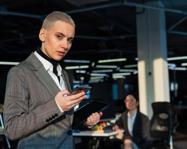 Kısa saçlı düşünceli genç kadın ofiste cep telefonu kullanıyor..