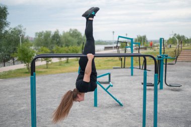 Şişman genç bir kadın açık hava barlarında jimnastik yapıyor.