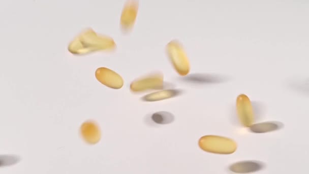 Närbild av fallande transparenta gula kapslar över vit bakgrund. Kosttillskott som innehåller omega 3 och fiskolja — Stockvideo
