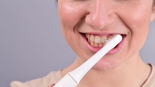 Retrato de cerca de una mujer caucásica cepillándose los dientes con un cepillo de dientes eléctrico. La niña realiza el procedimiento de higiene bucal matutina — Vídeo de stock