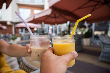 Bir adam ve bir kadın açık bir kafede içki bardaklarını tokuşturuyor. Randevudaki bir çiftin ellerinin yakın çekimi.