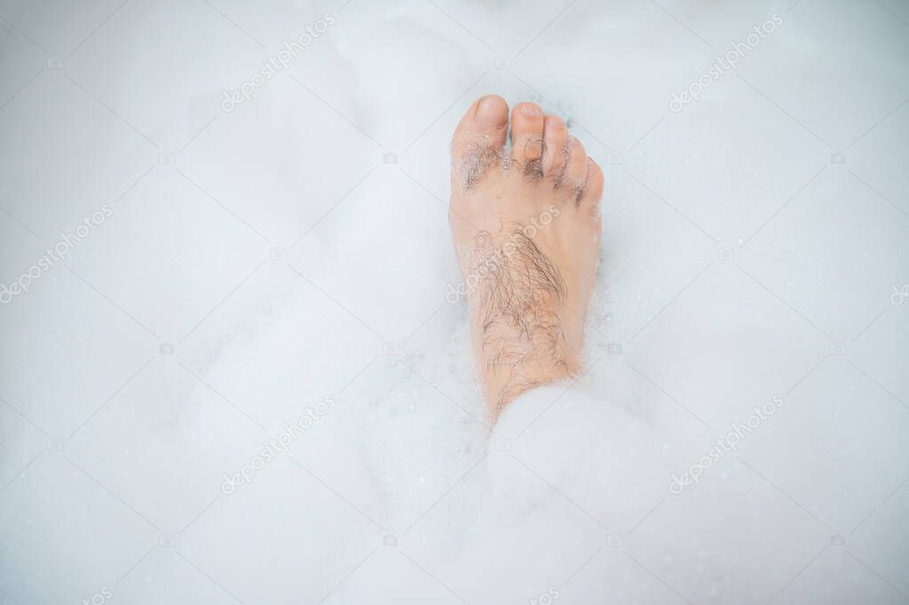 Funny picture of a man taking a relaxing bath. Close-up of male feet in a bubble bath