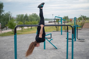 Şişman genç bir kadın açık hava barlarında jimnastik yapıyor.