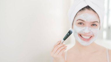 Saçında havlu olan güzel beyaz kadın kilden bir maske takıyor. Evdeki güzellikle ilgilenmek.