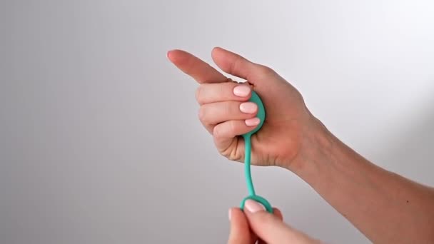 Faceless woman demonstrates a vaginal ball. Girl squeezes a kegel trainer with her hand for training pelvic floor muscles on a white background. — Stock Video