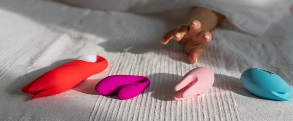 Kadın beyaz bir battaniyenin altında yatar ve vibratörlere uzanır. Kız ve seks oyuncakları yatak odasında.